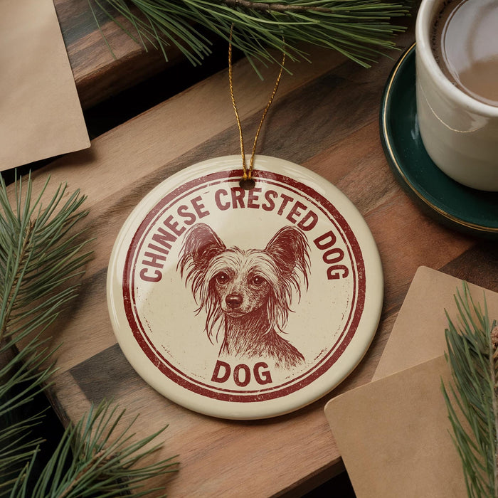 A round ornament featuring a Chinese crested dog, with the text "CHINESE CREsted DOG" printed on it, is displayed on a wooden surface alongside a cup of coffee and some pine branches.