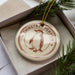 A round ornament with a penguin image and the text "CHINSTRAP PENGUIN" is displayed in a box, surrounded by pine branches.