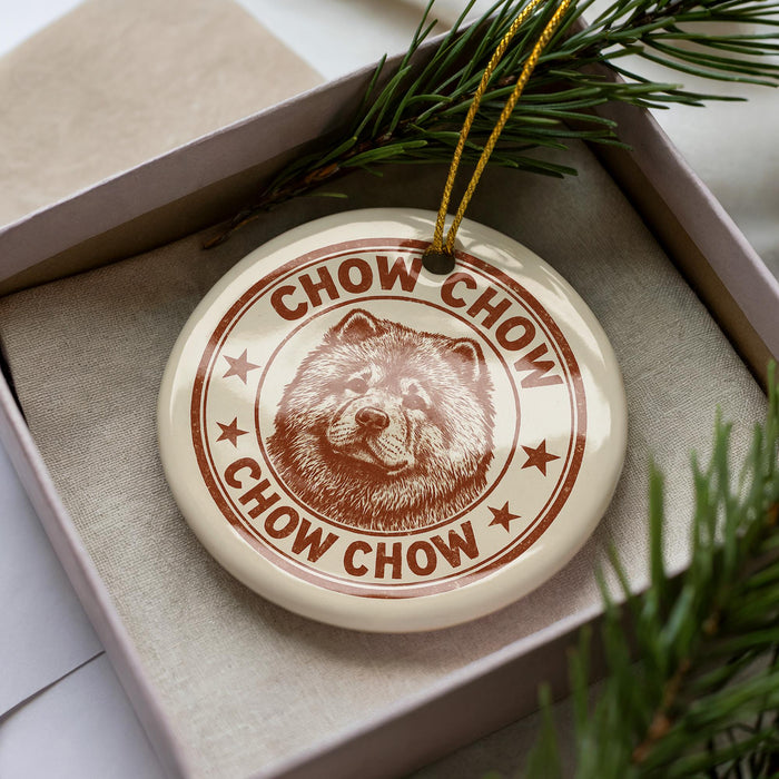A round ornament with a chow Chow dog image and the text "CHOW CHOW" printed on it, placed inside a box with pine branches.