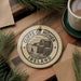 A circular ornament with the text "CLIFFS OF MOHER IRELAND" printed on it, surrounded by pine branches and a cup of coffee on a wooden surface.