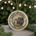 A circular ornament with the text "CLIFFS OF MOHER IRELAND" and an illustration of cliffs, hanging from a string against a background of Christmas lights and greenery.