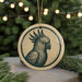 A round ornament featuring a parrot design is displayed in front of a blurred Christmas tree with twinkling lights.