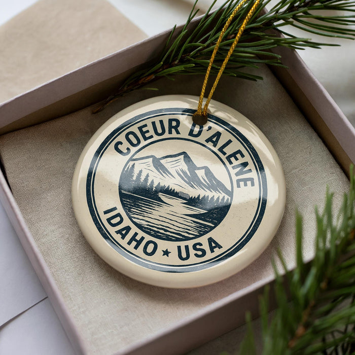 A decorative ornament in a box, featuring a mountain landscape and the text "COEUR DALENE IDAHO USA".