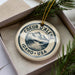 A decorative ornament in a box, featuring a mountain landscape and the text "COEUR DALENE IDAHO USA".