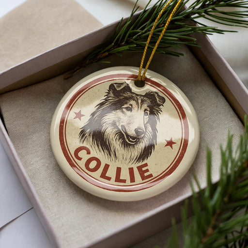 A round ornament with a picture of a dog's head and the name "COLLIE" written on it, placed inside a box with pine branches.