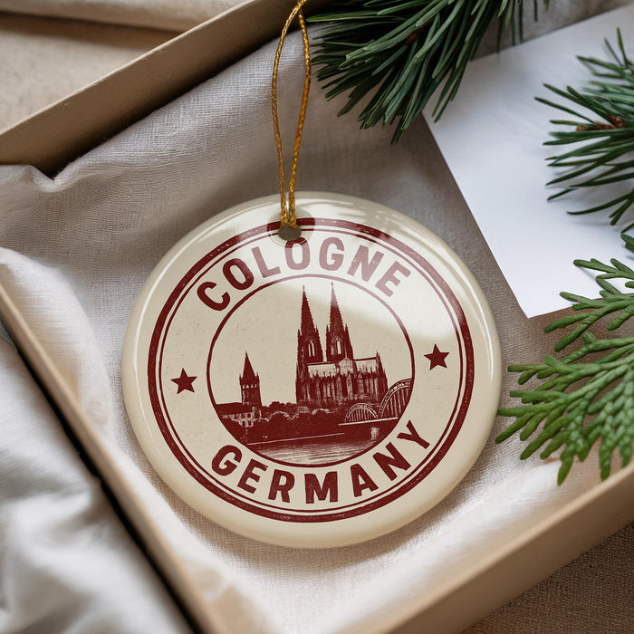 A round ornament with the text "COLOGNE GERMANY" and a graphic of a cathedral, hanging from a string.
