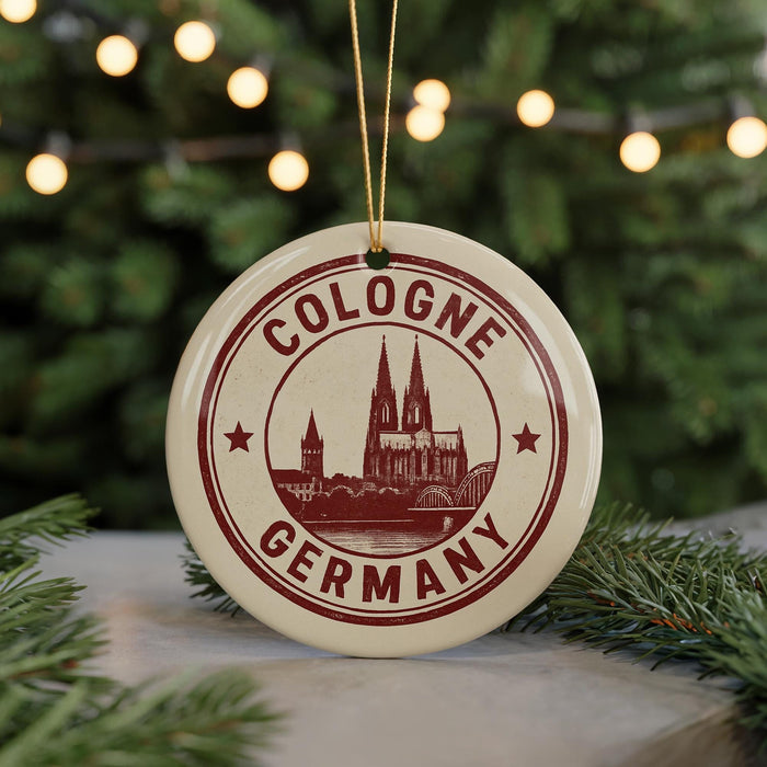 A circular ornament with the text "COLOGNE GERMANY" and an illustration of a cathedral, hanging from a string.