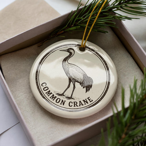 A ceramic ornament in the shape of a crane, with the text "Common Crane" printed on it, is displayed in a box with pine branches.