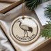 A decorative ornament featuring a black and white illustration of a crane, with the text "COMMON CRANE" printed on it, is displayed in a box with pine branches.