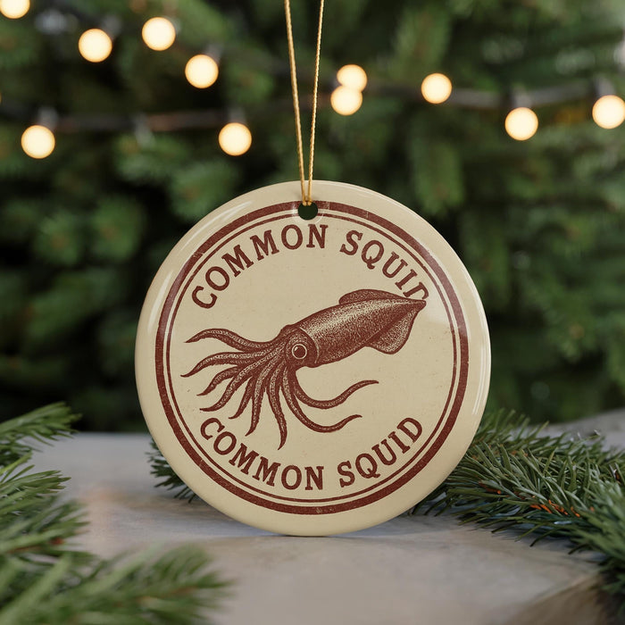 A round ornament with the text "COMMON SQUID" and an illustration of an octopus is displayed against a blurred background of Christmas lights and pine branches.