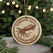 A round ornament with the text "COMMON SQUID" and an illustration of an octopus is displayed against a blurred background of Christmas lights and pine branches.