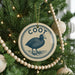A Christmas tree decorated with ornaments, including a circular ornament with a bird image and the word "Coot" written on it.