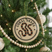 A round ornament with a black and orange snake design hangs from a Christmas tree, surrounded by white beads and greenery.