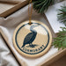 A circular ornament with a bird design and the word "Cormorant" printed on it, hanging from a string.