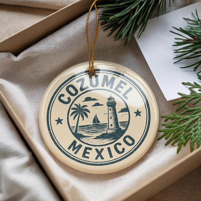 A circular ornament with the text "COZUMEL MEXICO" printed on it, surrounded by a lighthouse and palm trees, is displayed in a box with pine branches.