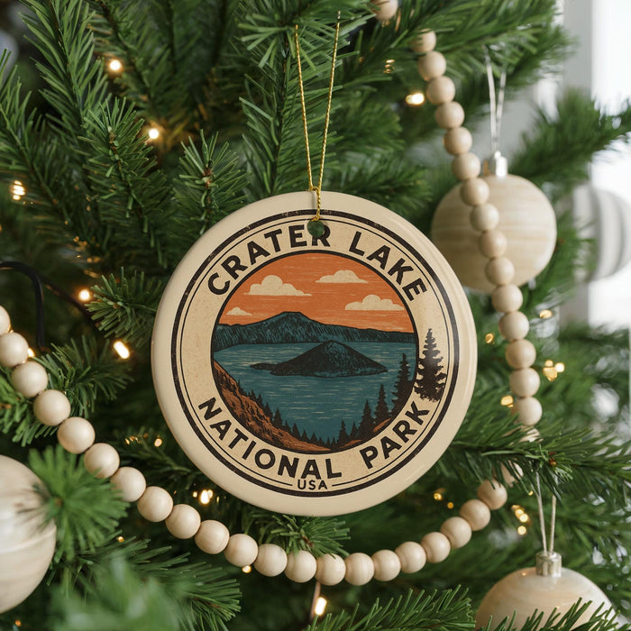 A circular ornament on a Christmas tree, featuring a scenic landscape with mountains and a lake, with the text "Crater Lake National Park" prominently displayed.