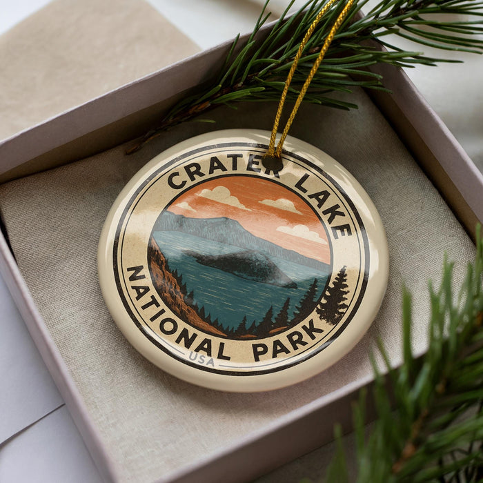 A circular ornament with the text "CRATER LAKE NATIONAL PARK" printed on it, surrounded by pine branches and pine needles.