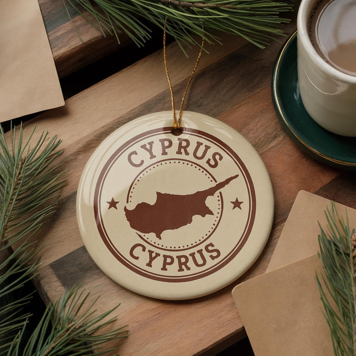 A circular ornament with the text "CYPRUS" and a map of the island of Cyprus, surrounded by pine branches and a cup of coffee on a wooden surface.