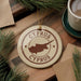 A circular ornament with the text "CYPRUS" and a map of the island of Cyprus, surrounded by pine branches and a cup of coffee on a wooden surface.