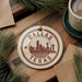 A circular ornament with the text "DALLAS TEXAS" and a silhouette of the Dallas skyline, hanging on a wooden surface.