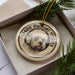 A decorative ornament featuring a Dandie Dinsmont Terrier dog, with the dog's face prominently displayed in the center of the ornament.