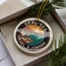 A circular ornament with the text "DEAU SEA ISRAEL JORDAN" on it, surrounded by pine branches.