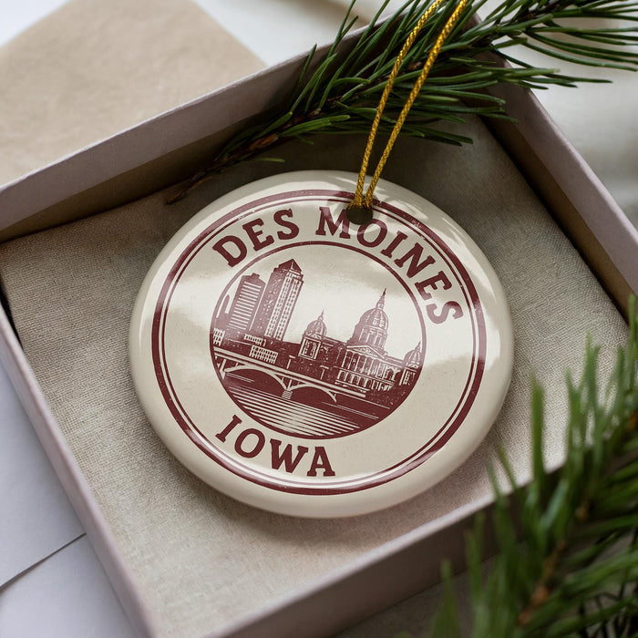 A decorative ornament in a box, featuring a circular design with a city skyline and the text "DES MOINES IOWA" printed on it.