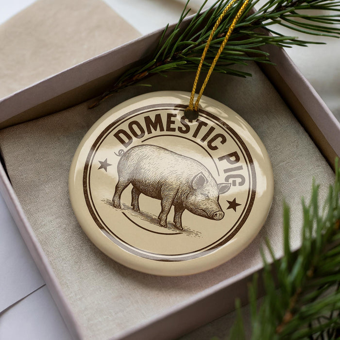 A decorative ornament featuring a pig illustration, placed in a box with pine branches.