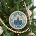A Christmas tree decorated with ornaments, including a circular ornament with the text "Dover DEWARRE" and a building illustration.
