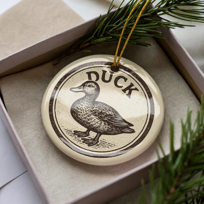 A ceramic ornament in a box, featuring a duck illustration and the word "DUCK" written on it.