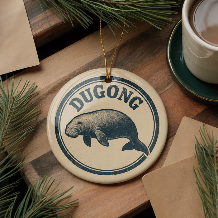 A round ornament with the word "DUGONG" and a drawing of a dugout is displayed on a wooden surface, surrounded by pine branches and a cup of coffee.