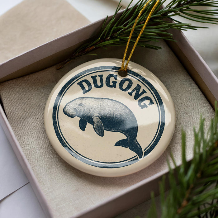 A round ornament with the word "DUGONG" printed on it, featuring a depiction of a dugout or dugout-like structure.