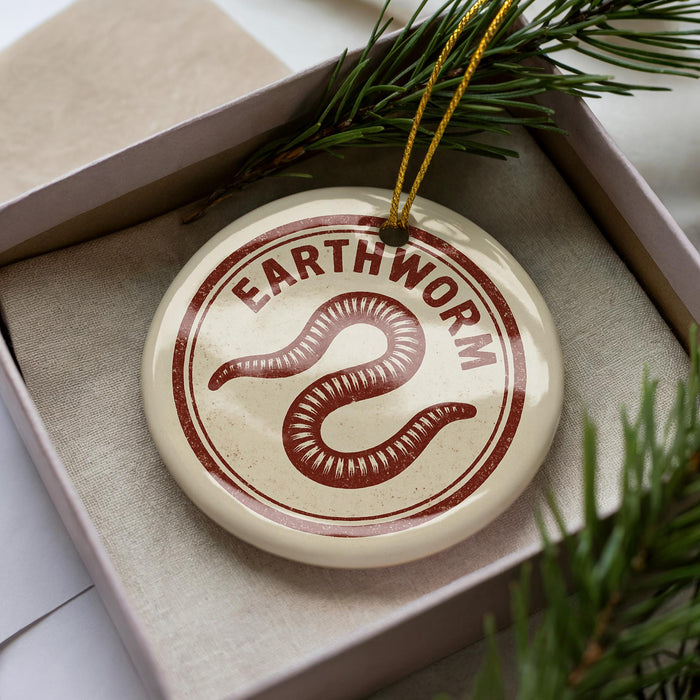 A circular ornament with the word "Earthworm" printed on it, placed inside a box with pine branches.
