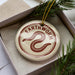 A circular ornament with the word "Earthworm" printed on it, placed inside a box with pine branches.