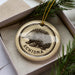 A circular ornament with a porcupine image and the word "ECHIDNA" printed on it, placed inside a box with pine branches.