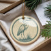 A decorative ornament featuring a heron is displayed in a box, surrounded by pine branches and greenery.