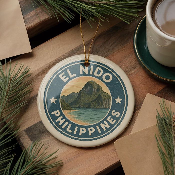 A circular ornament with the text "EL NIDO PHILIPPINES" and a scenic mountain landscape is displayed on a wooden surface, accompanied by a cup of coffee and pine branches.