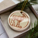 A circular ornament with a brown goat illustration and the word "ELAND" written on it, placed inside a box with pine branches.