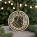 A circular ornament featuring a dog's head and the text "ESTRELLA MOUNTAIN DOG" is displayed on a table with pine branches in the background.