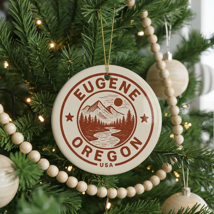 A Christmas tree decorated with ornaments, including a circular ornament with the text "EUGENE OREGON USA" and a mountain landscape design.