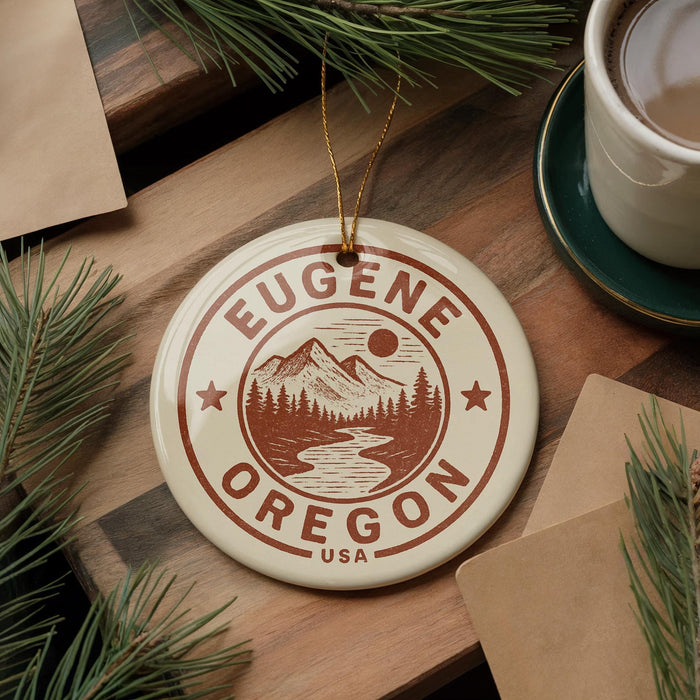 A circular ornament with the text "EUGENE OREGON USA" printed on it, surrounded by pine branches and a cup of coffee on a wooden surface.
