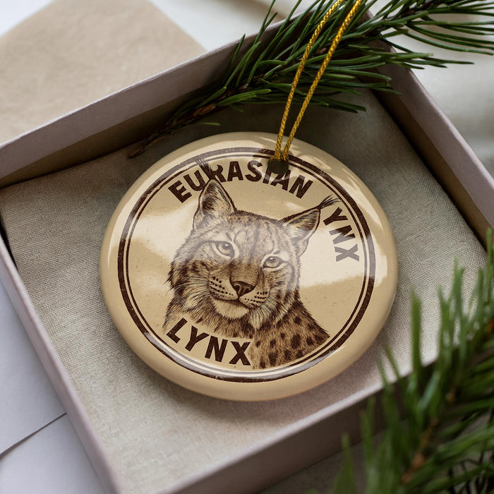 A circular ornament with a picture of a lynx on it, placed inside a box with pine branches.
