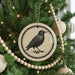 A Christmas tree decorated with ornaments, including a circular ornament featuring a black bird illustration.