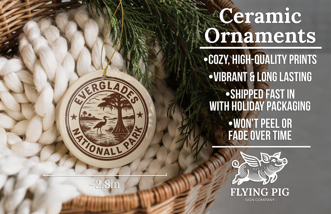Ceramic ornaments, featuring a round ornament with a tree design and text, hanging from a wicker basket with pine branches.