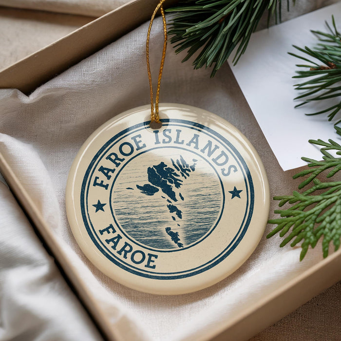A round ornament with the text "Faroe Islands Faroe" and a map of the Faroe Islands, placed in a box with pine branches.