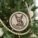 A ceramic ornament featuring a fennec fox is hanging on a Christmas tree, surrounded by other ornaments and lights.