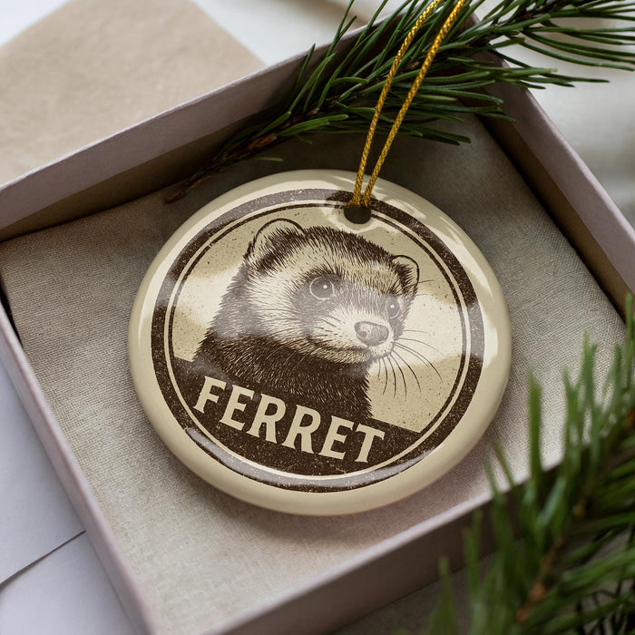 A round ornament with a ferret image and the word "FERRET" printed on it, placed inside a box with pine branches.