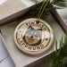 A circular ornament featuring a dog's face with the text "FINISH LAPPHUND" around it, placed in a box with pine branches.