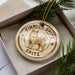 A circular ornament with a dog image and the text "Finnist Spitz" printed on it, placed inside a box with pine branches.