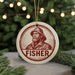 A round ornament with a portrait of a man wearing a hat and a coat, with the word "FISHER" written below the portrait.